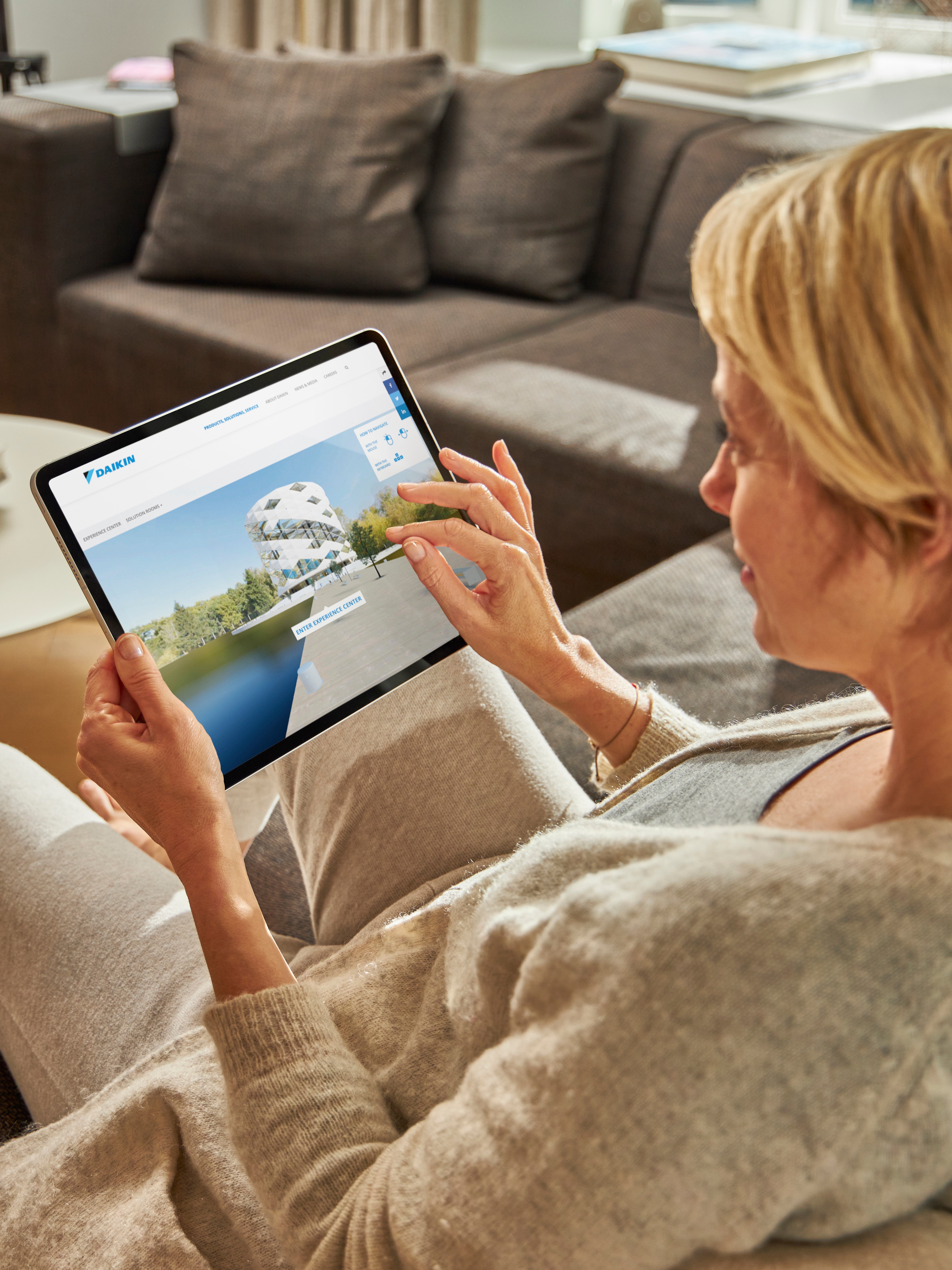 Mulher sentada num sofá visualiza os sistemas de ar condicionado no centro de experiência virtual no seu tablet