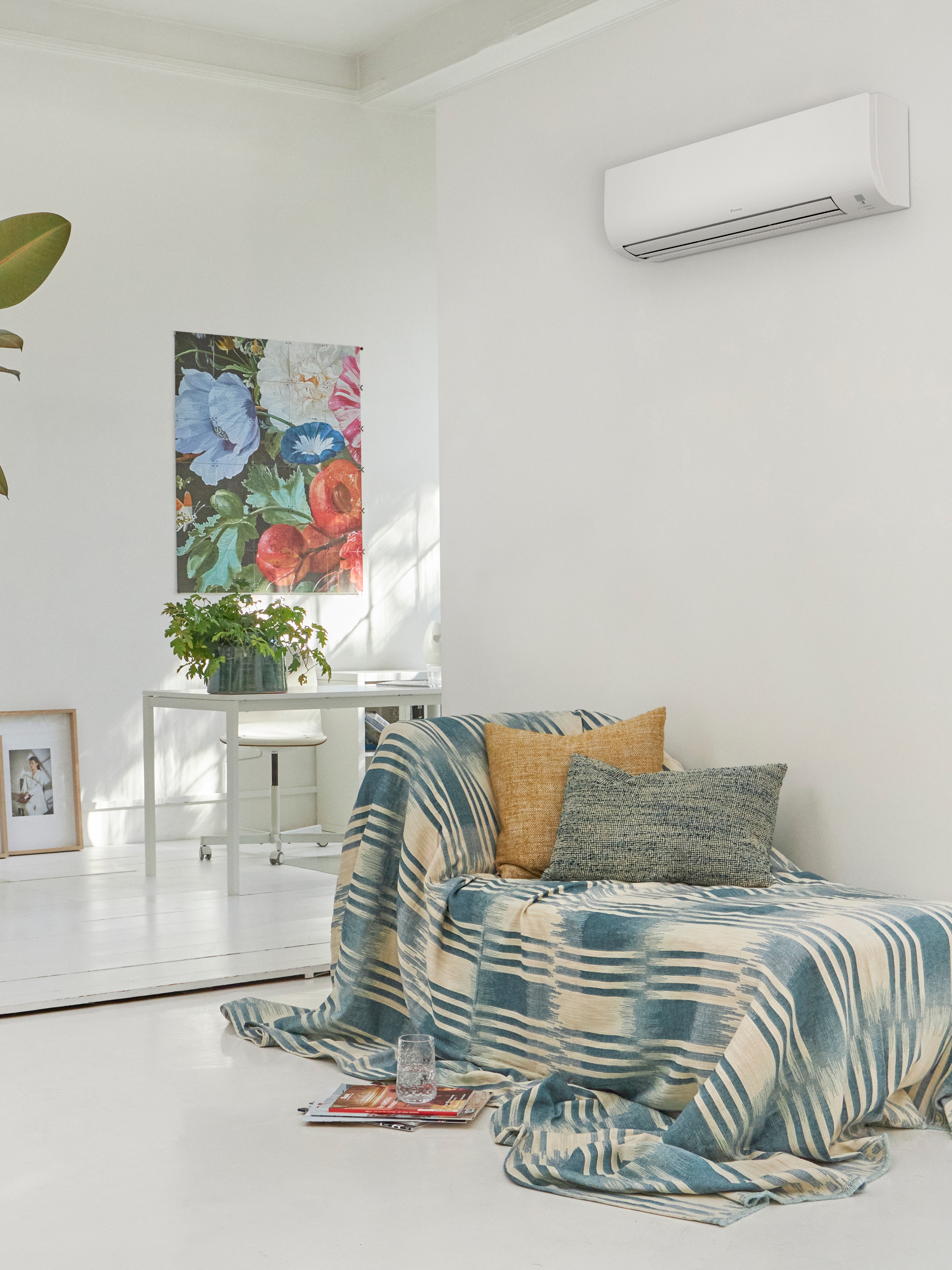 Sala de estar branca com um sofá e uma solução de climatização mural acima do mesmo