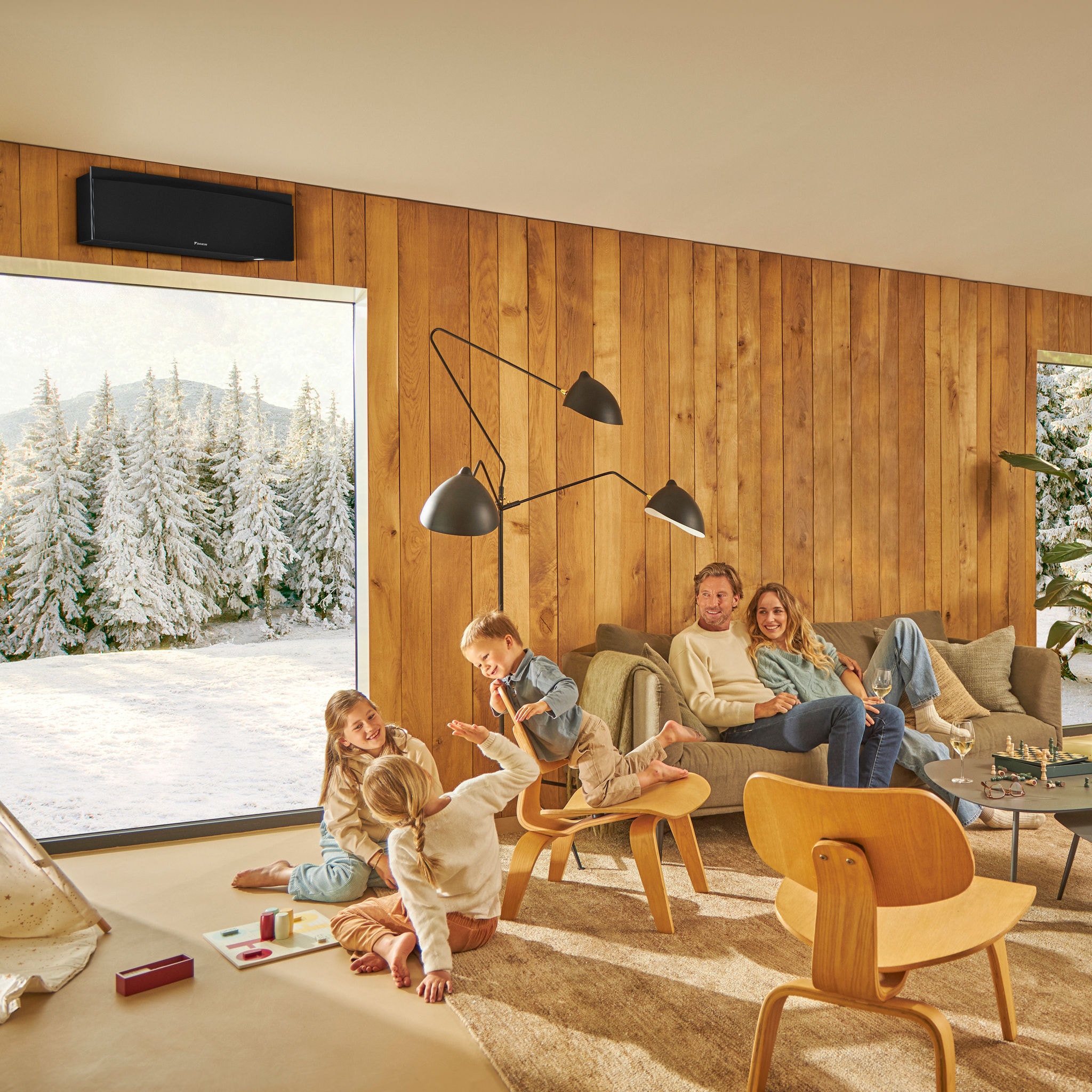 Família a usufruir de uma sala de estar quente e acolhedora com uma paisagem de inverno em segundo plano, demonstrando a eficácia das nossas soluções de aquecimento, arrefecimento e ventilação para criar um ambiente interior confortável durante todo o ano