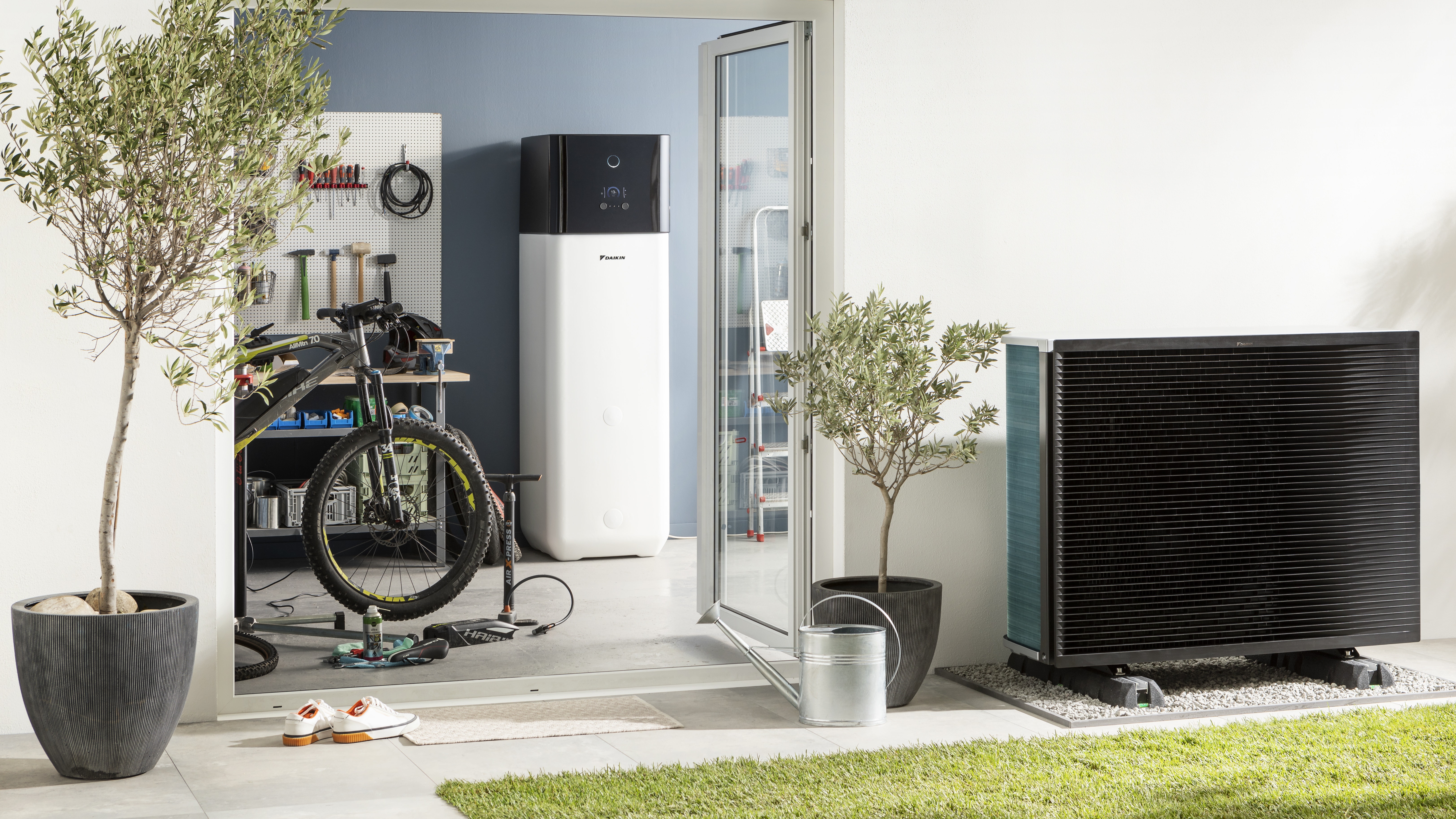 Unidade interior de bomba de calor ar-água com depósito de água quente integrado instalada numa habitação e unidade exterior no jardim