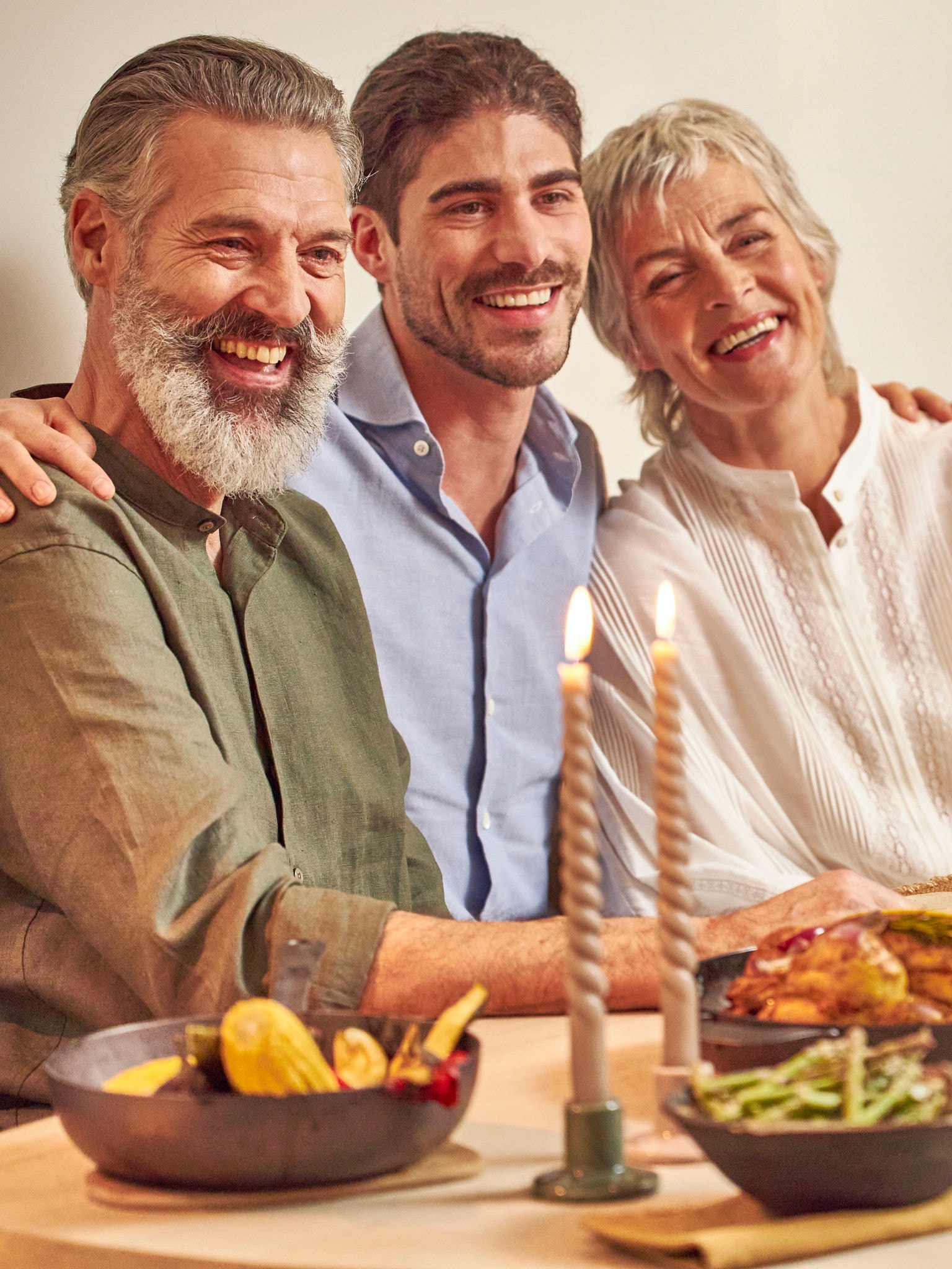 Filho adulto com os seus pais, felizes, sentados à mesa de jantar