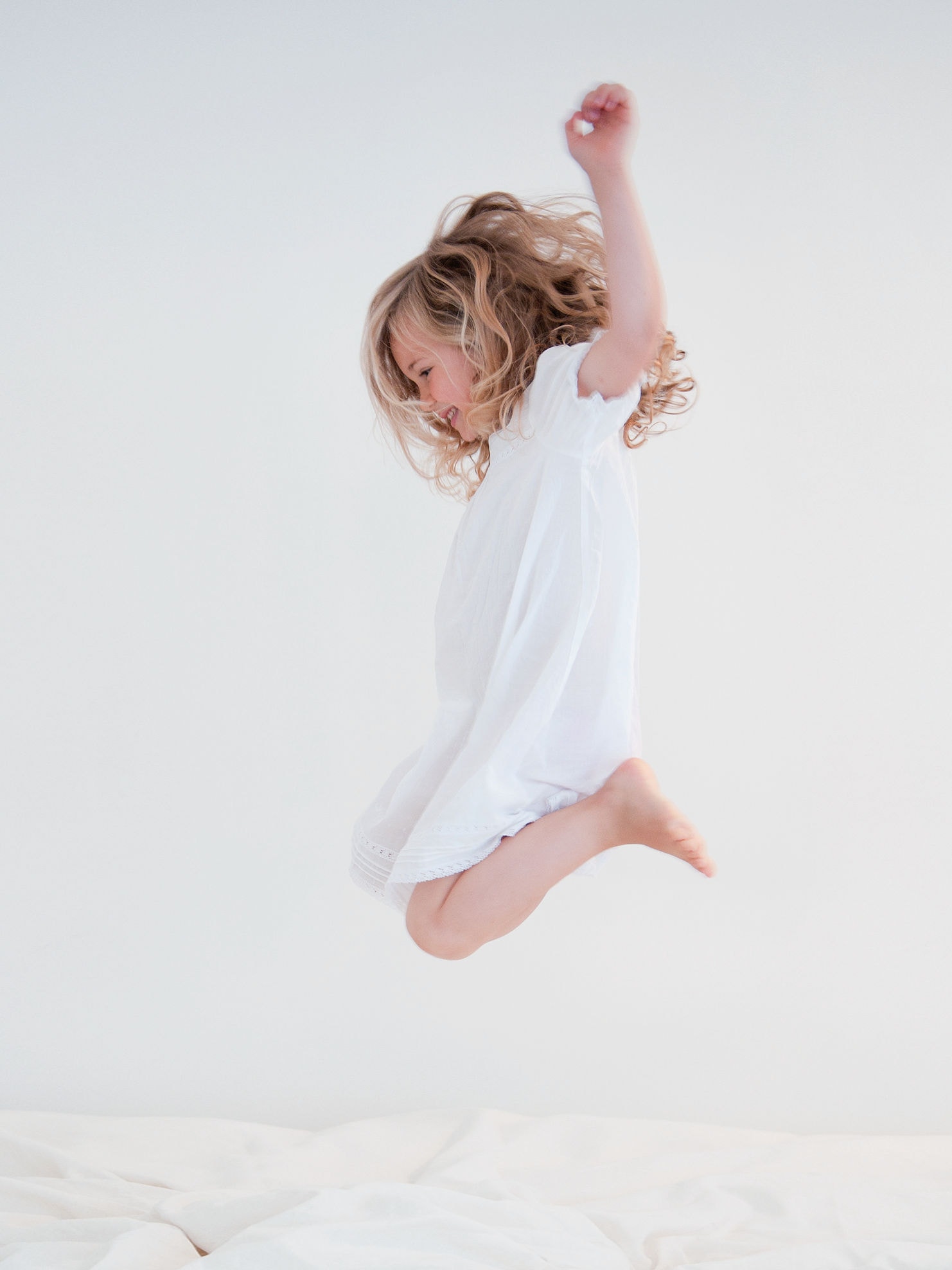 Menina com um vestido branco salta numa cama branca